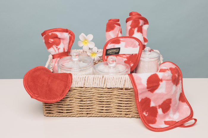 Wicker basket with red and white patterned potholders, oven mitts, and glass containers on a light gray background.