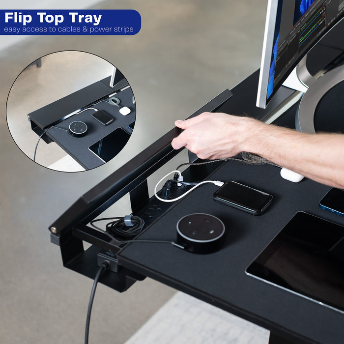 Desk with flip top tray for cable management and power strips, showing a hand plugging in devices.
