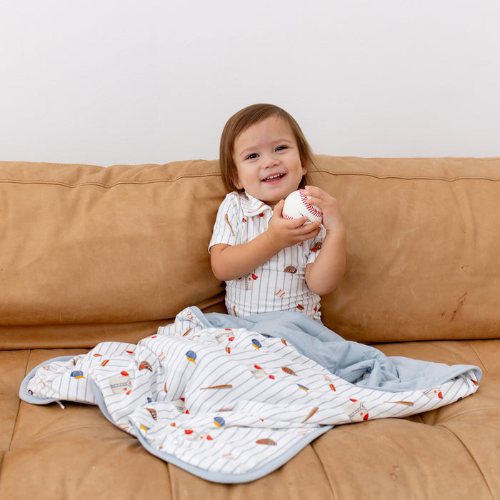 Young boy sitting on a couch holding a baseball with the Baby Blanket in Home Run over his legs