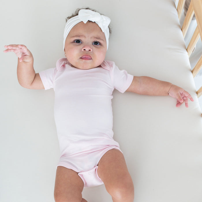 Infant wearing Kyte Baby short Bodysuit in Sakura pink