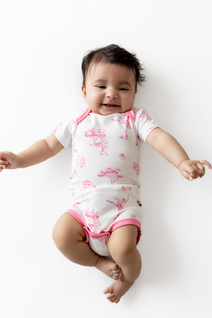 Smiling infant laying on a white surface wearing the Bodysuit in Toile Ballet