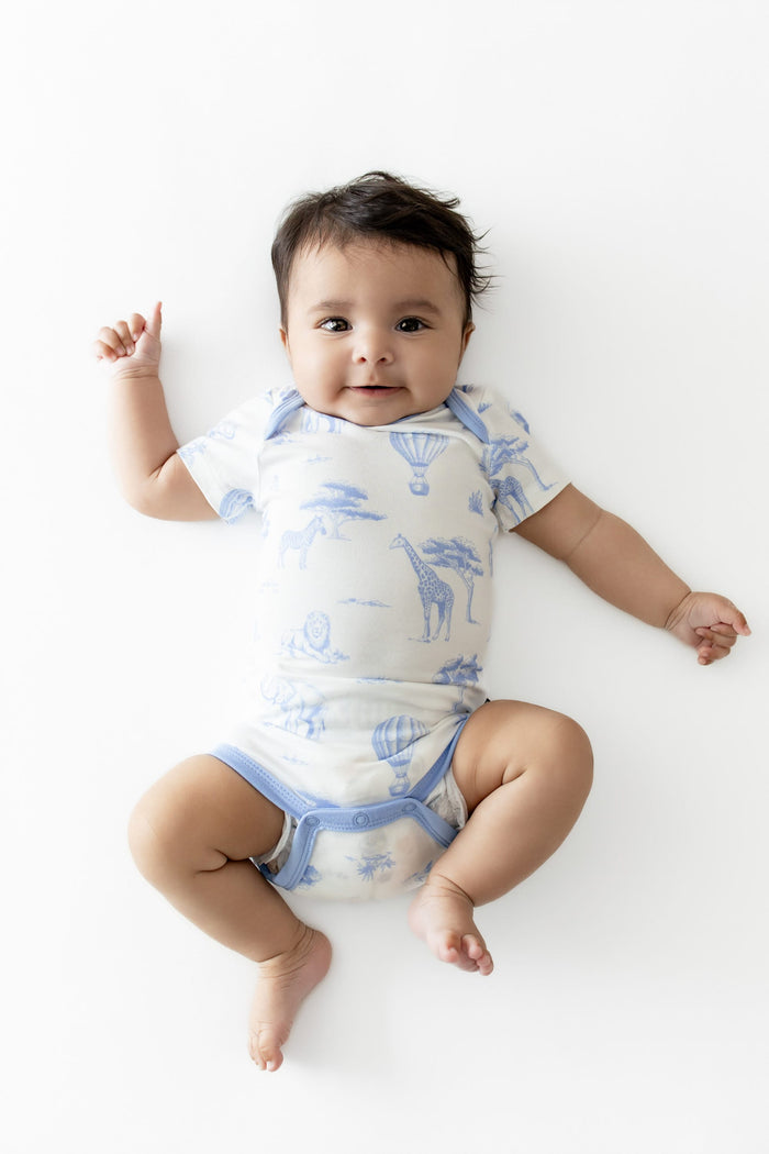 Infant laying on a white surface wearing the Bodysuit in Toile Safari