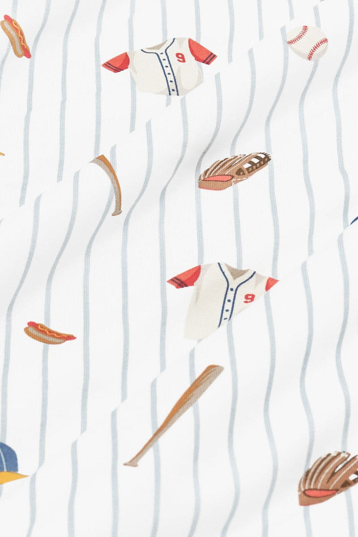 Close up of bamboo fabric: An all-over print featuring baseballs, wooden baseball bats, catcher’s mitts, white baseball jerseys with red sleeves and a red number 9, blue baseball caps with a yellow brim, and a hot dog, over a white background with dusty blue pinstripes.
