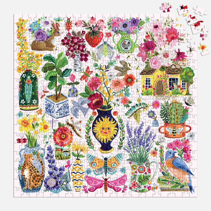 The Buzzy Bouquets 500 Piece Puzzle by Jennifer O Lewis/August Wren features vibrant illustrations of flowers, plants, vases, a cottage, butterfly, birds, and garden objects. Several pieces are missing in the top right corner.