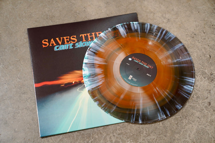 A limited edition Saves The Day Can’t Slow Down vinyl, featuring a striking black/orange splatter LP, lies atop its album sleeve on a textured gray surface.