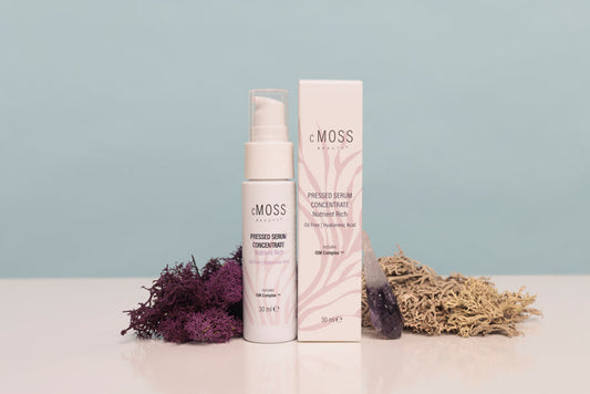 eMOSS Protected Serum Concentrate shown with its white pump bottle and matching rectangular box on a white surface, styled with dried purple and beige botanicals against a pale blue background.