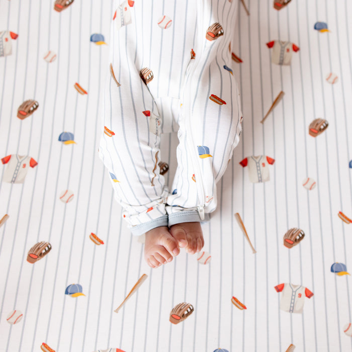 The zipper closure on the leg of the Zippered Romper in Home Run shown on an infant model laying on a Crib Sheet in Home Run