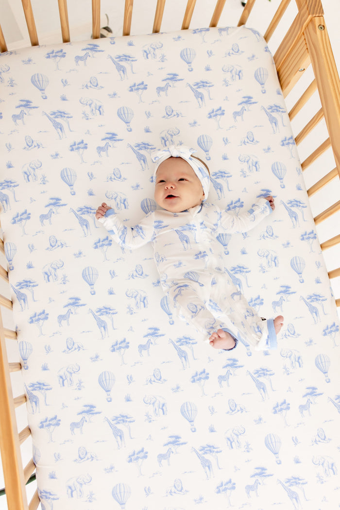 Infant laying in a crib on a Crib Sheet in Toile Safari wearing the matching zippered romper and bow