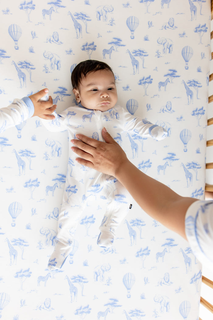 Infant laying in a crib on top of the Crib Sheet in Toile Safari wearing the matching zippered footie