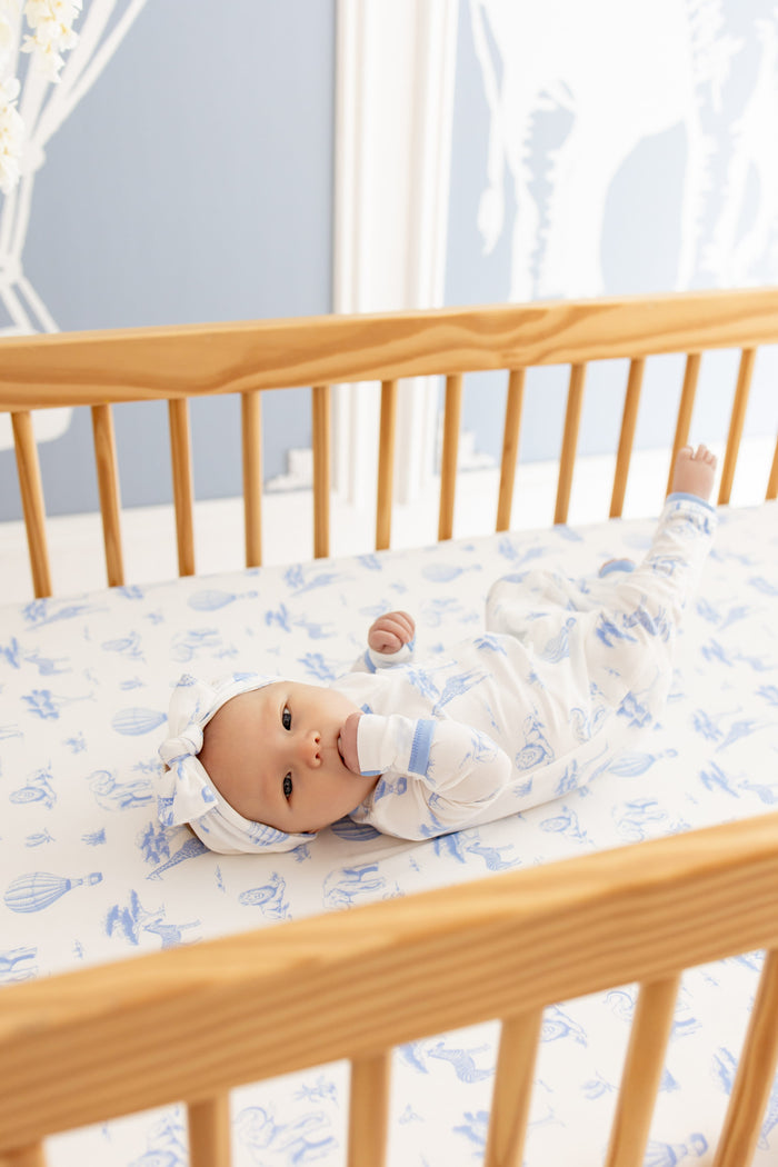 Infant laying in a light wooden crib on top of a Crib Sheet in Toile Safari