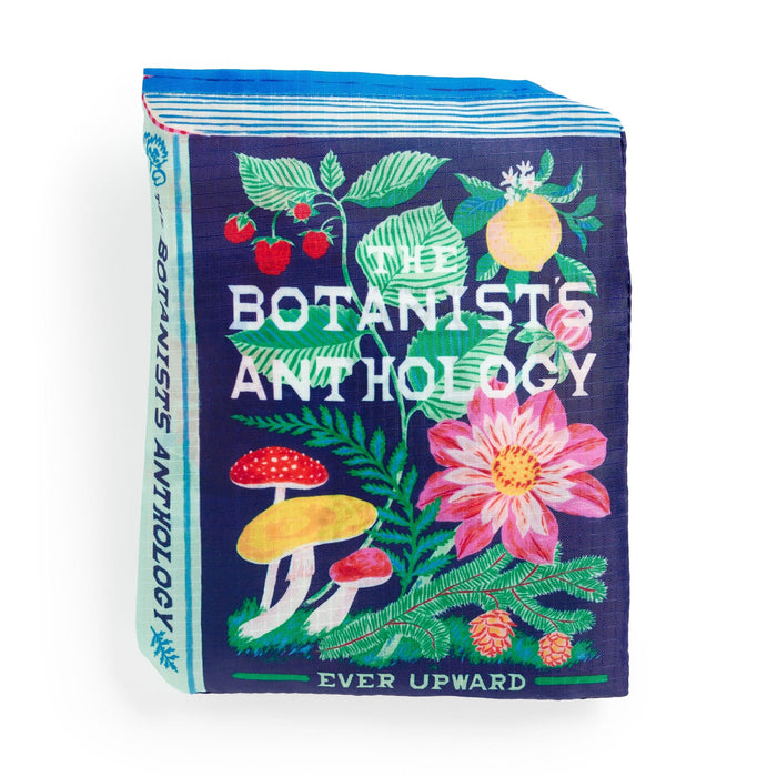 A colorful, book-shaped Ever Upward Botanist Bookshelf Packable Nylon Tote Bag by Emily Taylor features mushrooms, leaves, strawberries, and a large pink flower on a dark blue background. The spine reads "Botanists Anthology" and the bottom says "Ever Upward.