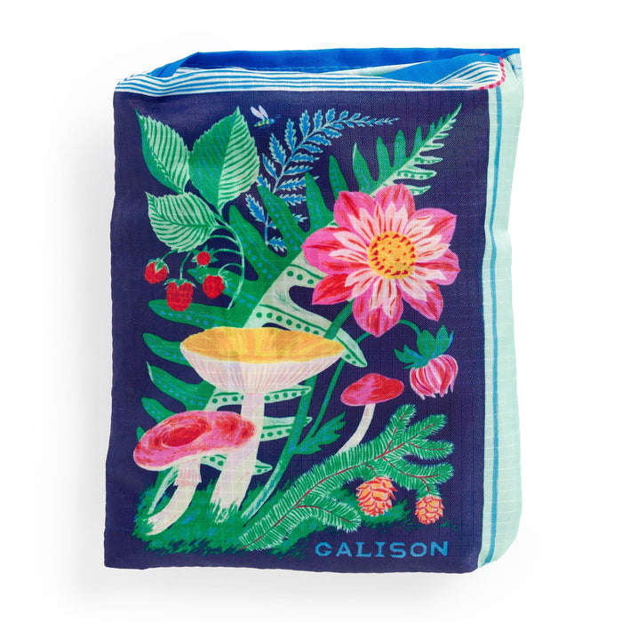 The Ever Upward Botanist Bookshelf Packable Nylon Tote Bag by Emily Taylor features colorful mushrooms, pink flowers, strawberries, and green leaves on a dark blue background with light blue striped sides and a blue interior.