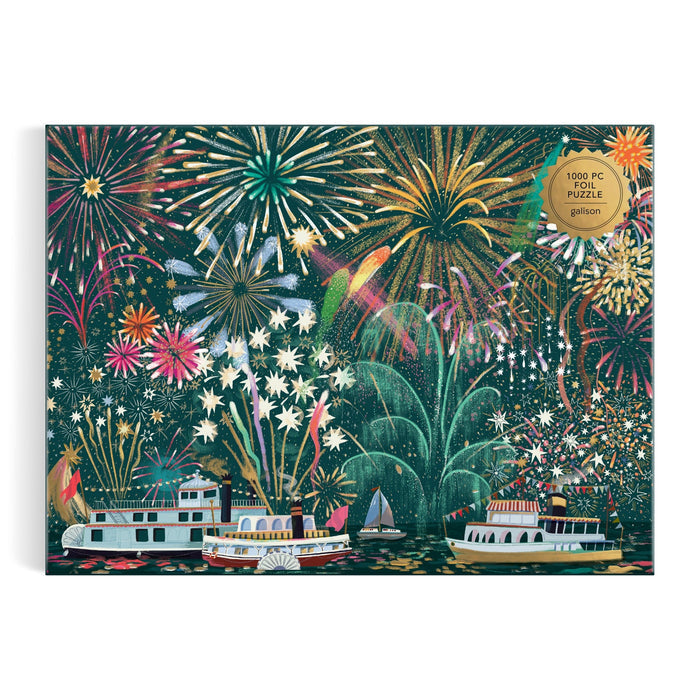 The "Fireworks Jubilee 1000 Piece Foil Puzzle" by Sarah Long features colorful fireworks lighting up the night sky above riverboats, with reflections shimmering on the water.