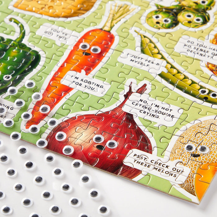 The Brass Monkey Googly Food 1000 Piece Puzzle features illustrated vegetables with playful speech bubbles and googly eyes, plus a sheet of unused googly eyes in the corner for extra fun in this quirky food-themed collage.