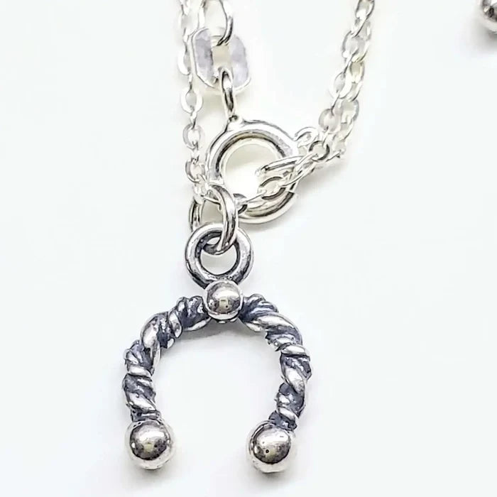 Handmade sterling silver horseshoe jewelry pendant on a chain, showcasing artisan craftsmanship and charm.