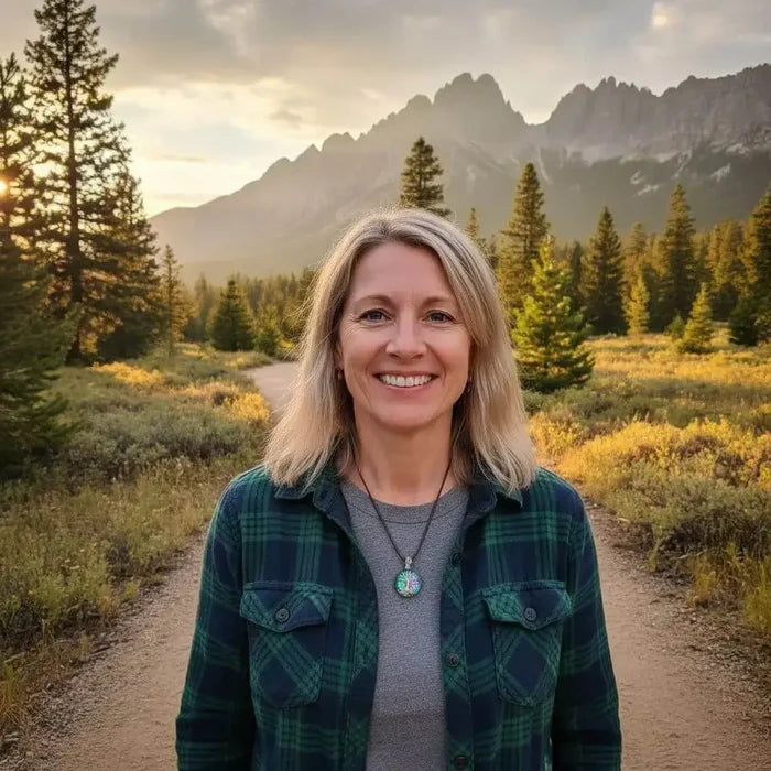 Woman standing outdoors wearing a handmade tree of life dichroic pendant necklace in a scenic mountain landscape.