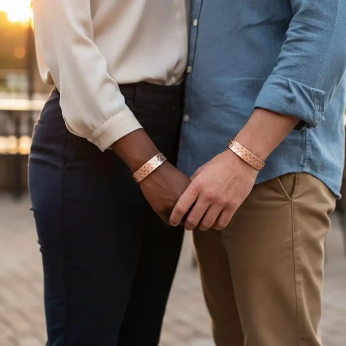 His and Her Copper Embossed Weave Cuffs 16 Gauge worn by a couple holding hands outdoors in a romantic setting.
