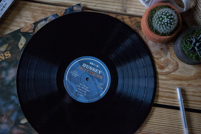 A limited pressing Hussey vinyl LP rests on a wooden table beside small potted plants and its record cover.
