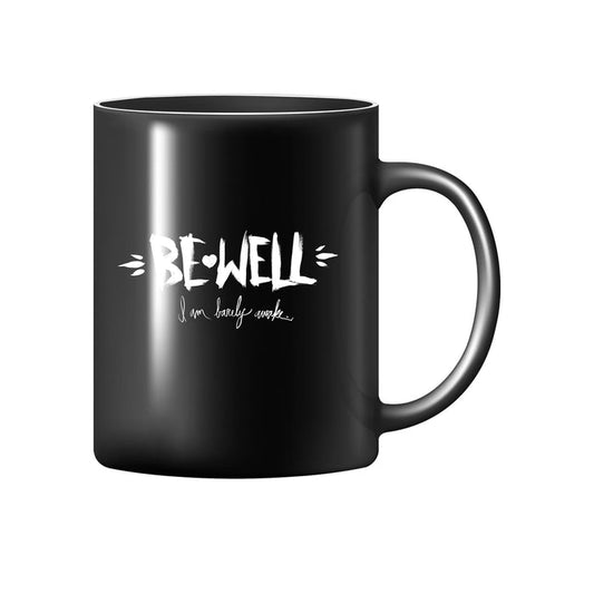 A Be Well black coffee mug featuring "BE-WELL" in bold white letters and "I am lovely awake" in cursive appears on a plain white background.