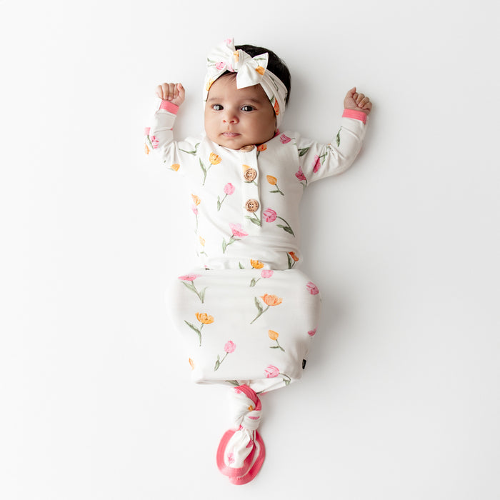Young infant wearing the Knotted Gown with Bow Set in Tulip laying on a white surface