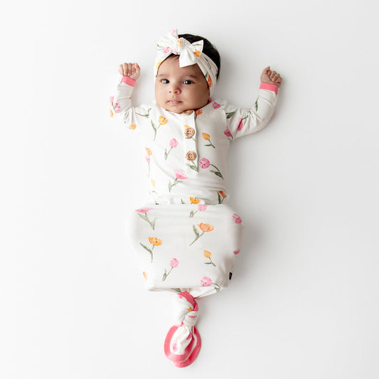 Young infant wearing the Knotted Gown with Bow Set in Tulip laying on a white surface