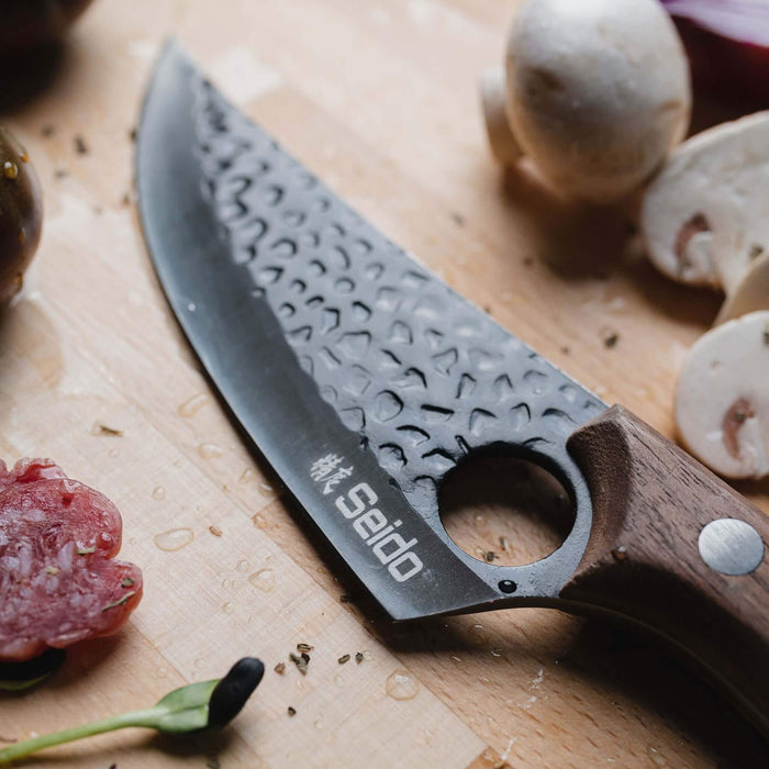 Knife with a wooden handle and textured blade on a cutting board with ingredients