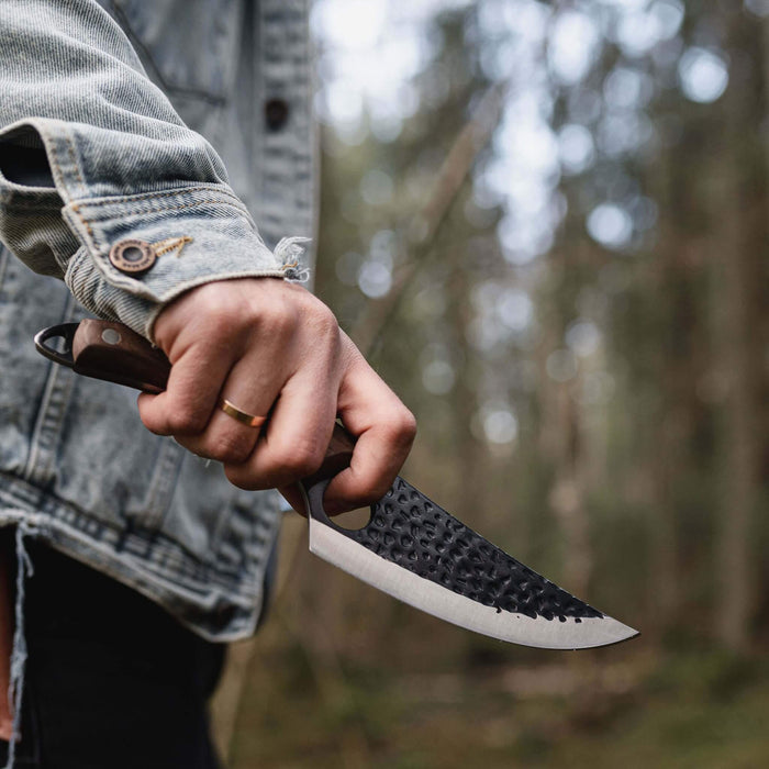 Person holding a knife with a textured blade in a forest setting