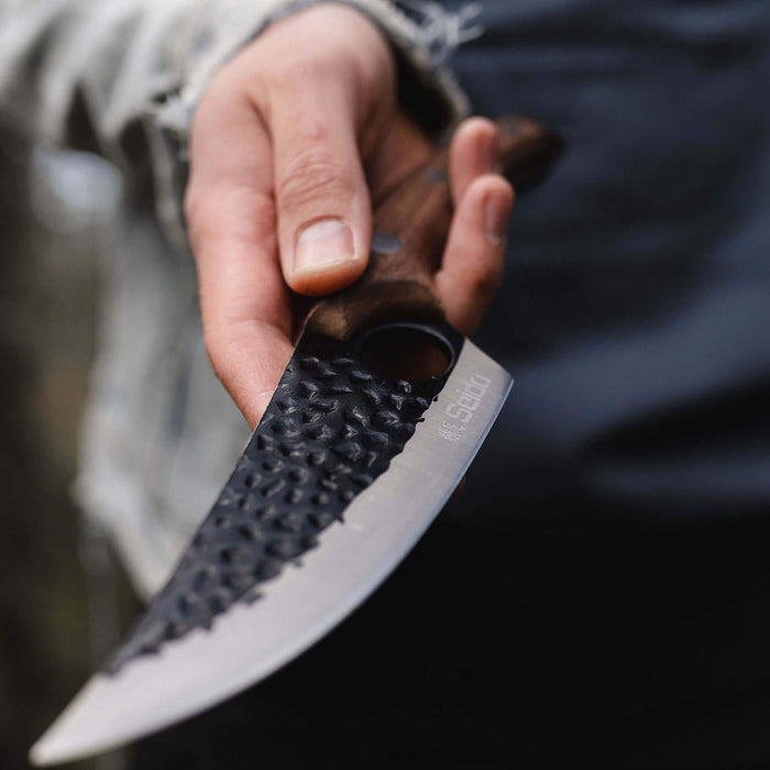 Hand holding a knife with a textured blade and wooden handle, blurred background