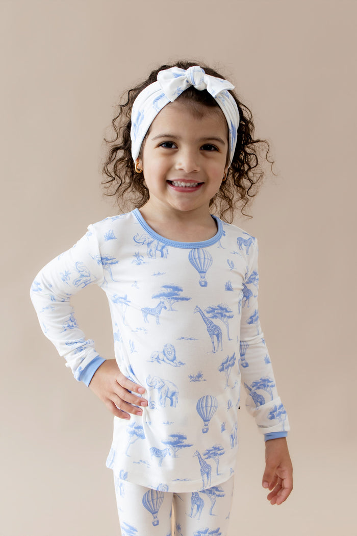 Young girl posing wearing the Long Sleeve Pajamas in Toile Safari with matching bow
