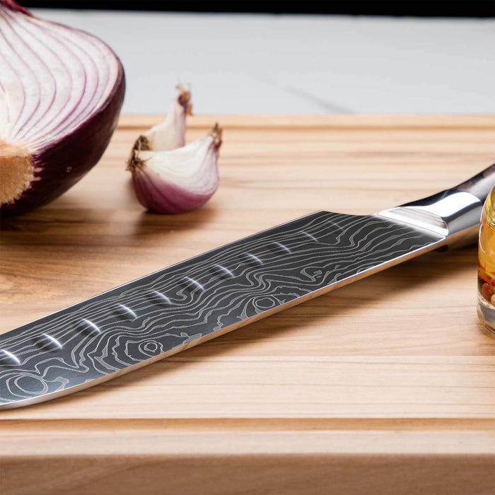 Knife with a decorative blade on a wooden cutting board next to an onion and garlic.