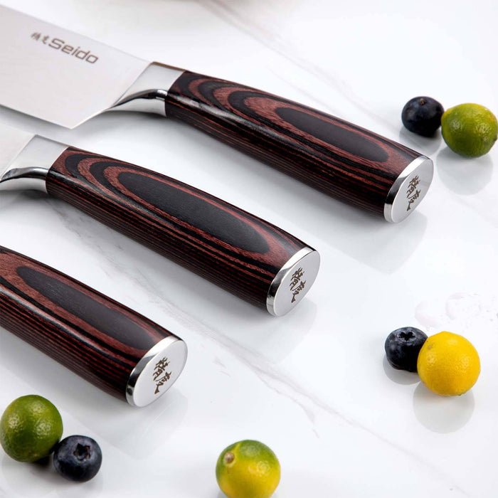 Set of three knives with wooden handles on a white surface with fruits.