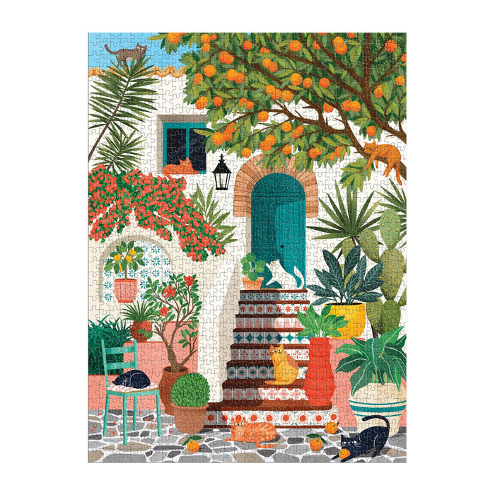 The Mediterranean Cats 1000 Piece Puzzle by Tània Garcia features a vibrant courtyard scene with potted plants, orange trees, and cats lounging by a turquoise door against a white building.