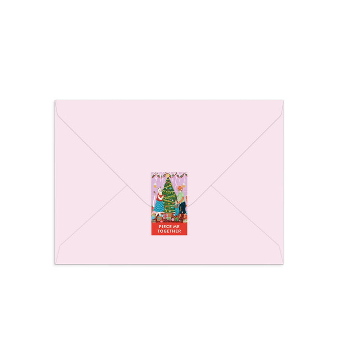 A light pink envelope sealed with a festive sticker features the Joanna Clay Meowy Christmas Greeting Card Puzzle, showcasing a charming feline-themed illustration and the words PIECE ME TOGETHER on a red background.