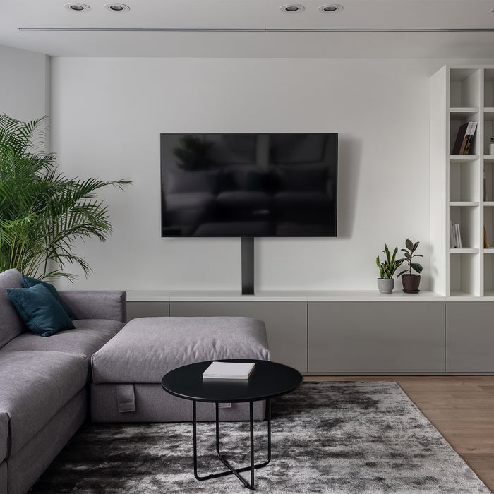 Modern living room with a gray sectional sofa, round black coffee table, and wall-mounted TV.