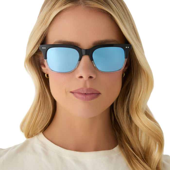 on model - female wearing diff eyewear x fantastic four featuring the mr. fantastic square sunglasses with a black to clear frame and quantum blue mirror polarized lenses front view