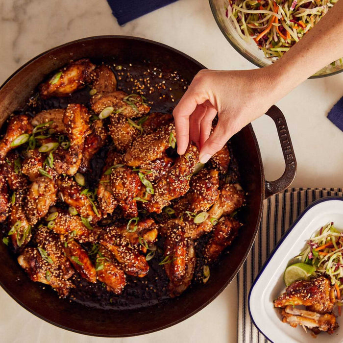 Smithey No. 14 dual handle skillet lifestyle image with hand grabbing a wing from the skillet full of wings