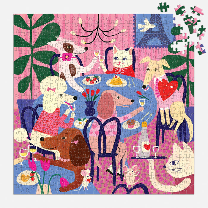The Paws for Love 500 Piece Puzzle by Anne Bentley features six dogs enjoying food and drinks in a cozy pink room with plants. Some pieces are missing in the upper right corner.