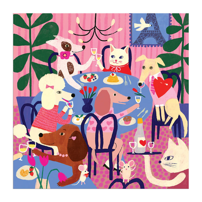 The Paws for Love 500 Piece Puzzle by Anne Bentley showcases six dogs and a cat celebrating around a dining table with food, flowers, and an Eiffel Tower picture in the background.