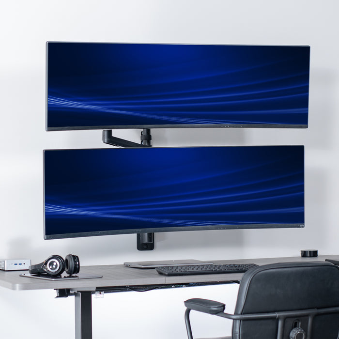 A black pneumatic arm dual ultrawide monitor wall mount holding two monitors in an office setting.