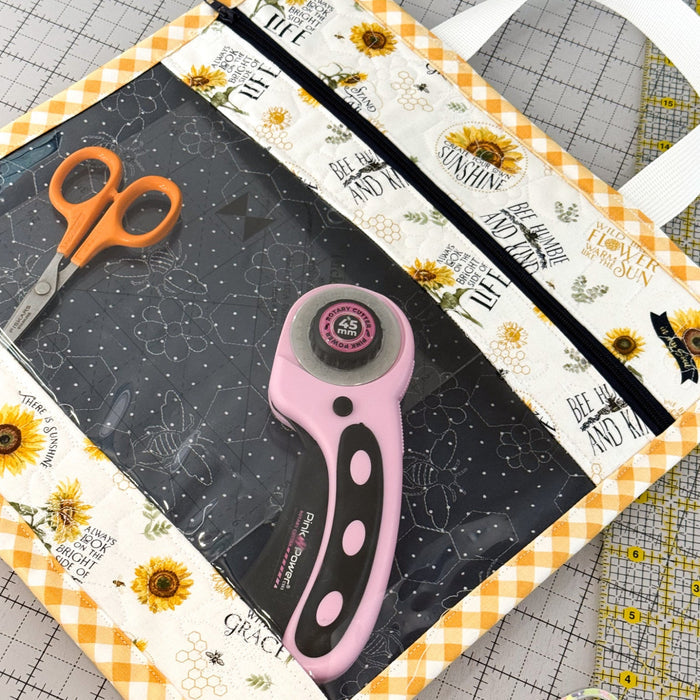 Crafting tools including a rotary cutter and scissors on a cutting mat with sunflower design.