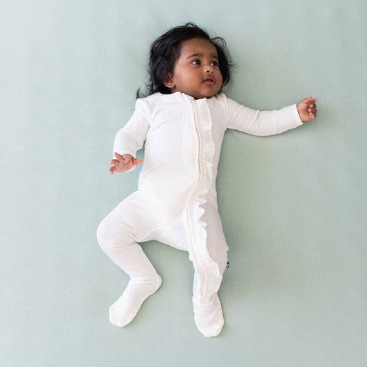Infant wearing Kyte Baby Ribbed Ruffle Zipper Footie in Cloud