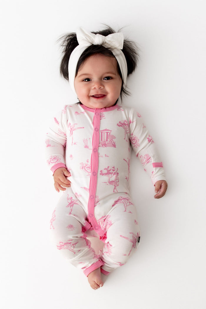 Smiling infant wearing the Romper in Toile Ballet with a white bow