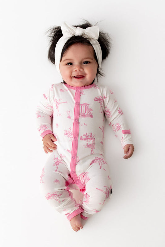 Smiling infant wearing the Romper in Toile Ballet with a white bow