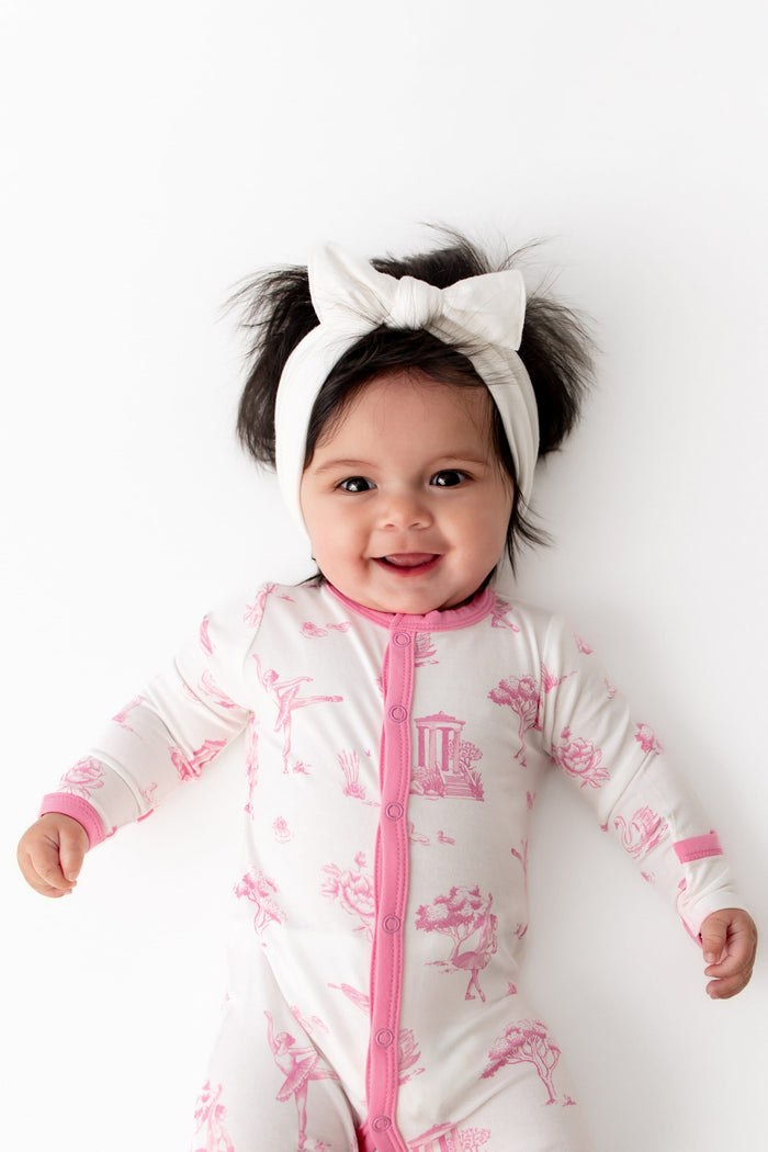 Close up of infant wearing the Romper in Toile Ballet paired with a white bow