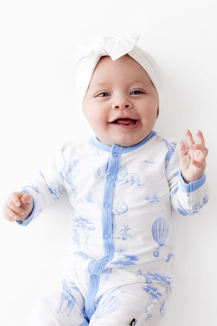 Close up of smiling infant wearing the Romper in Toile Safari with a white bow