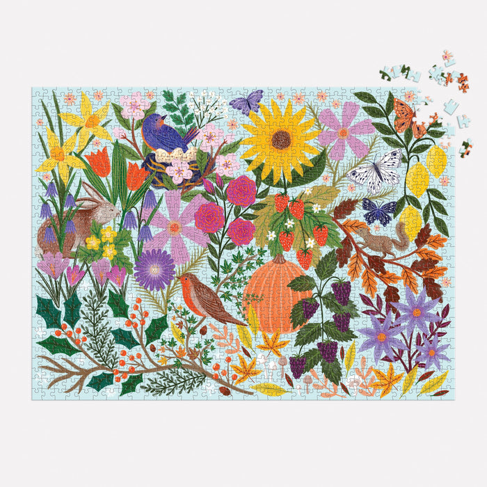 The Lee Foster-Wilson Seasons in Bloom 1000 Piece Puzzle features a lively floral, fruit, bird, and butterfly design with an unfinished section in the top right and several loose pieces waiting to be placed.