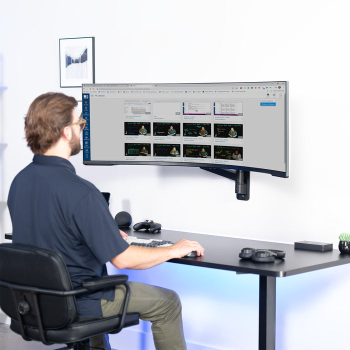 Model sitting at desk with single ultrawide monitor mounted to wall.