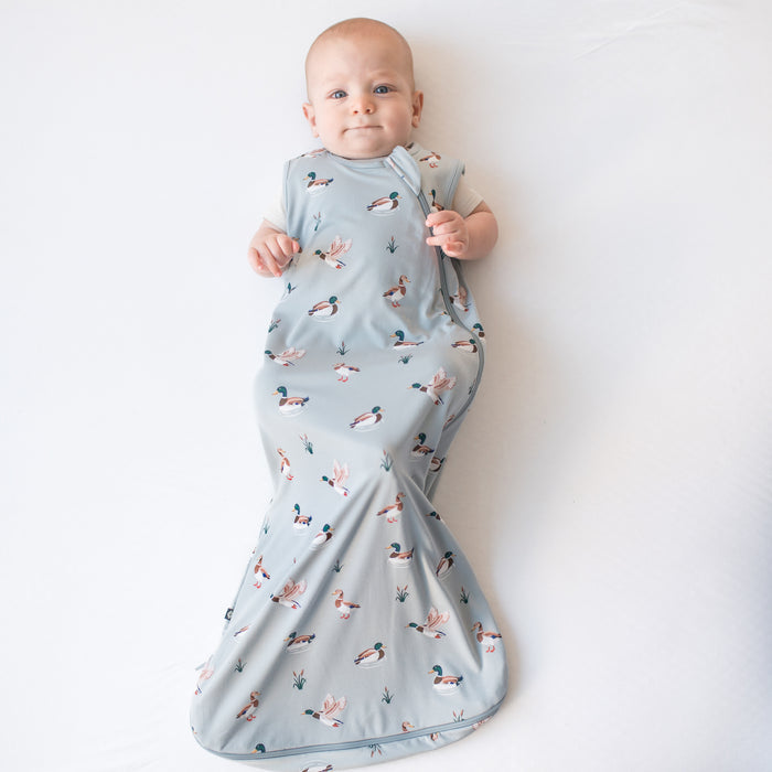 Infant laying on a white surface wearing the Sleep Bag in Mallard