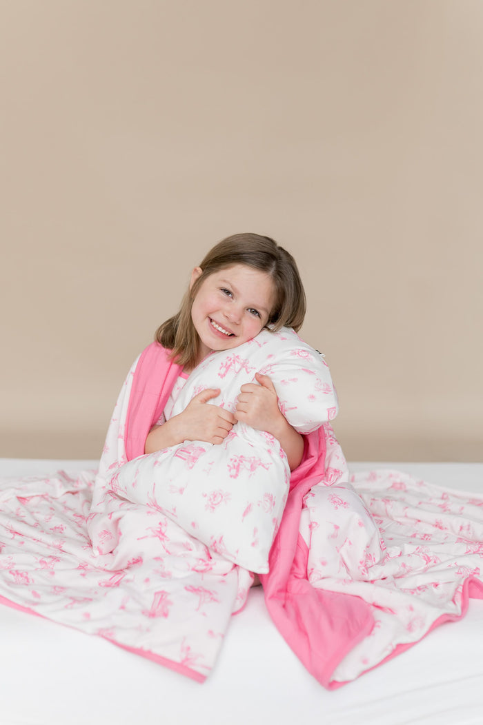 Young girl holding the Standard Pillowcase in Toile Ballet on a pillow with the matching blanket wrapped around her