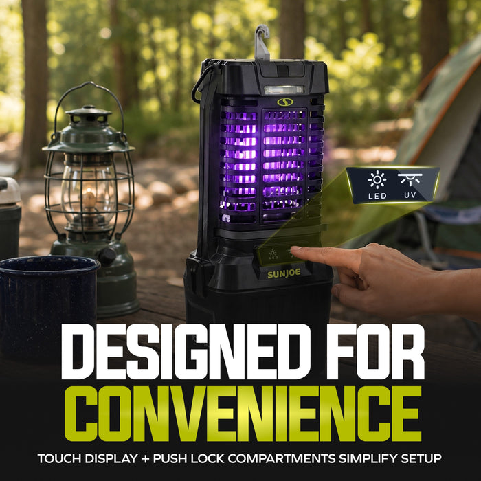 A black outdoor fly trap light with a glowing purple LED UV light chamber, shown on a table in a campsite setting with a lantern, cup, and tent in the background. A hand is touching the front display.